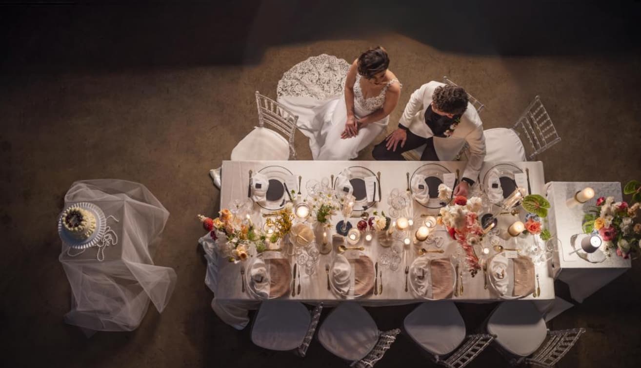 A bride and groom at a candlelit, flower-dressed wedding table at Eikendal, seen from above